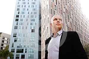 Serious caucasian man wearing suit standing next to office buildings. Copy space.