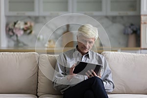 Serious Caucasian older retired man using tablet computer