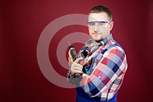 serious Caucasian repairman in goggles holding woodworking tools. Carpenter portrait on red studio background