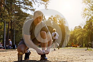 Serious caucasian young sportsman lacing sneakers standing on knee