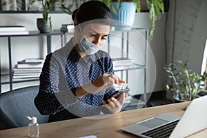 Serious cautious young indian ethnicity woman cleaning mobile phone screen.