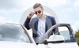 Serious CEO in formal wear and sunglasses getting into his automobile at downtown area of modern city