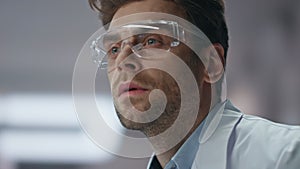 Serious chemist thinking research wearing safety glasses in laboratory close up