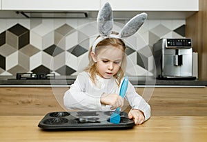 Serious child in bunny ears lubricate baking dish with silicone brush
