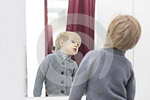 Serious Child - European blond boy tries on clothes in a store in the dressing room and looks at himself in the mirror