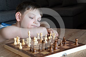 The serious child lost in thought playing chess. Playing board games, on coronavirus quarantine. The child playing chess