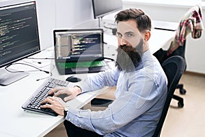 Serious computer programmer developer working in IT office, sitting at desk and coding, working on a project in software