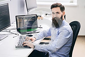 Serious computer programmer developer working in IT office, sitting at desk and coding, working on a project in software
