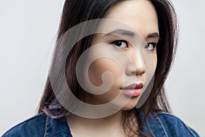 Serious concentrated beautiful young brunette woman with makeup and long hair, looking at camera.