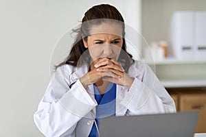 Serious concentrated mature woman doctor looking at laptop screen