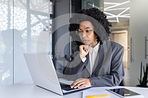 Serious concentrated and thinking businesswoman inside office at workplace typing on laptop, female boss working with