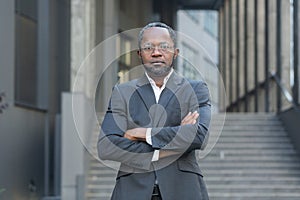 Serious and confident African American man in business suit looking at camera, businessman with crossed arms outside
