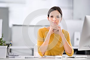 Serious, confident and ambitious business woman sitting at her desk while resting her chin on her hands. Portrait of a