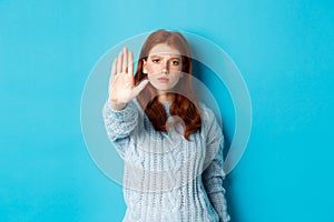 Serious and confident redhead girl telling to stop, saying no, showing extended palm to prohibit action, standing over