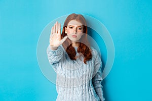 Serious and confident redhead girl telling to stop, saying no, showing extended palm to prohibit action, standing over photo