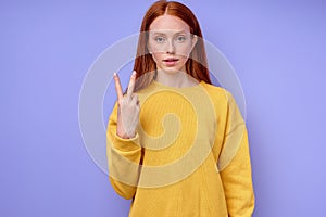 serious confident redhead woman in yellow stylish sweater demonstrating letter V