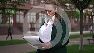 Serious confident successful overweight businesswoman analyzing graphs standing on city street sidewalk. Portrait of