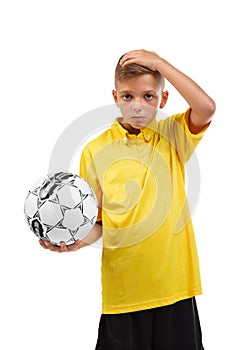 Serious, confused boy with a soccer ball holding his head isolated on a white background. School activities concept.