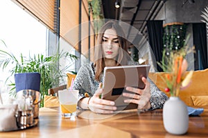 Serious and confused young woman typing on tablet, chatting, maintains a blog. Freelancer work in cafe modern coworking