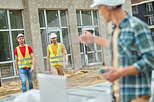 Serious construction workers in reflective waistcoats approaching their colleague