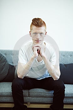 Serious contemplation. A red haired man sitting on a couch looking directly at the camera.