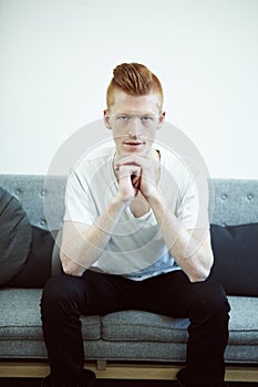 Serious, couch and portrait of man with ginger hair or sit in a lounge in thought or for hipster fashion and against