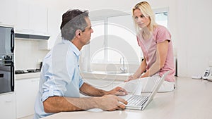 Serious couple with laptop sitting in kitchen