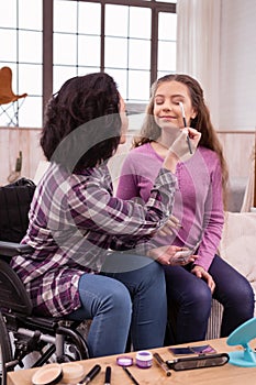 Serious crippled woman helping girl with makeup