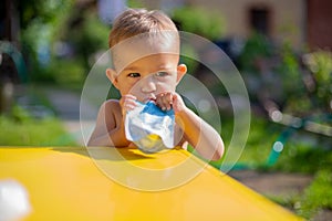 serious cute baby girl eating fruit puree in pouch and looking into the camera in front of the yellow table. on the