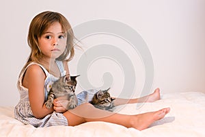 Serious, cute girl holding tabby kittens on soft off-white comforter