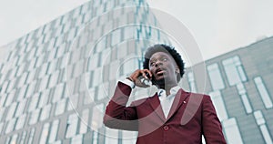 Serious dark-skinned businessman dressed in suit is standing outside in front of glass building of company, corporation
