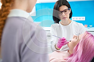 Serious dentist conducts thorough examination oral cavity of young patient