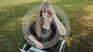 Serious disabled young caucasian woman in wheelchair in the park stroking her hair on the autumn breeze