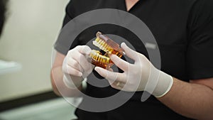 Serious doctor with glasses showing human jaws model with dental braces to patient in clinic