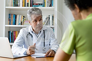 Serious doctor with gray hair talking with patient