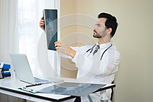 Serious doctor holding and checking a patient`s x-ray film in th