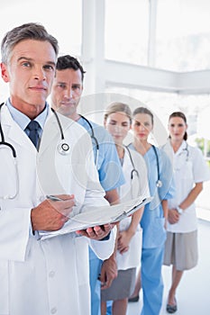 Serious doctor holding clipboard and standing in front of his me