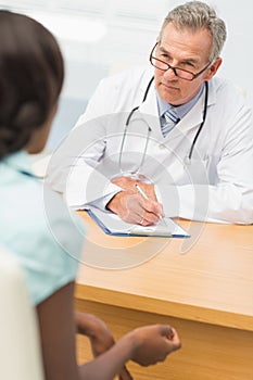 Serious doctor listening to his patient and taking notes