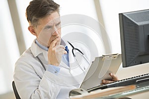 Vážný lékař kouká na počítač zatímco držení schránky na 