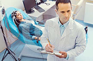 Serious doctor taking notes during electroencephalography procedure photo