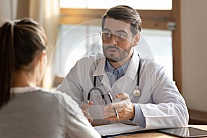 Serious doctor wearing glasses consulting female patient at medical appointment