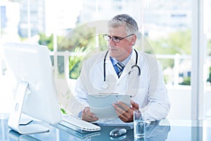 Serious doctor working on computer at his desk