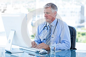 Serious doctor working on computer at his desk