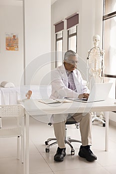 Serious elderly Indian practitioner man working at laptop