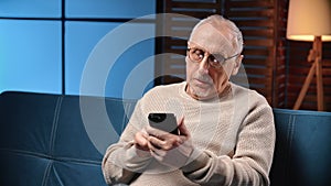 Serious elderly man using modern smartphone, portrait of retiree person with mobile gadget at home