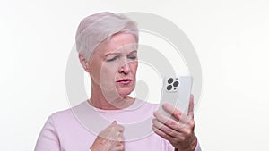 Serious Elderly Woman Displeased with News on Phone Against White Background