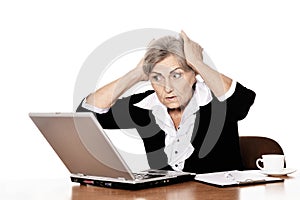 Serious elderly woman doctor sitting at table with computer