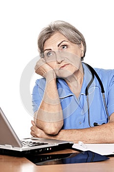 Serious elderly woman doctor sitting at table with computer isolated