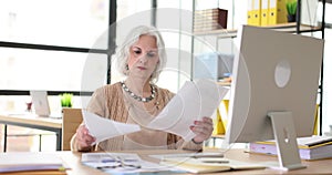 Serious elderly woman holding documents and checking information