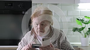 Serious elderly woman shopping online with credit card using mobile cell phone at home